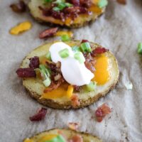 one potato bite on parchment paper with bacon, cheese and sour cream