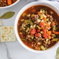 vegetable beef soup in bowl with saltine cracker and bay leaf
