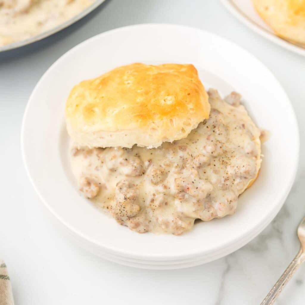 Sausage Gravy on a white plate with a biscuit.