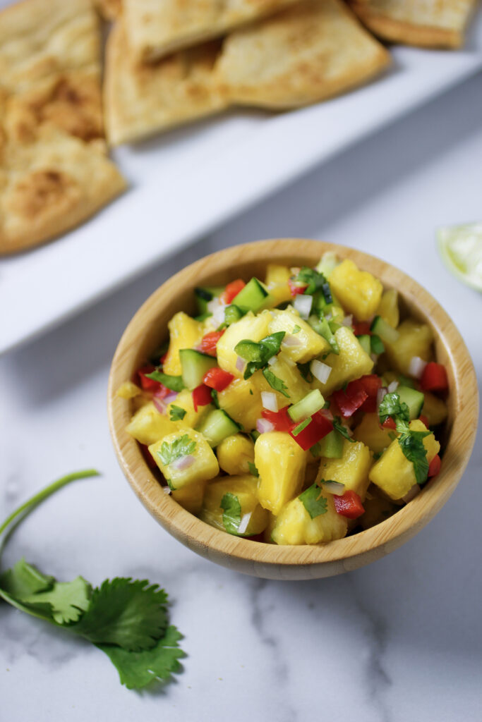 pineapple salsa in wooden bowl with pita chips, cilantro and lime
