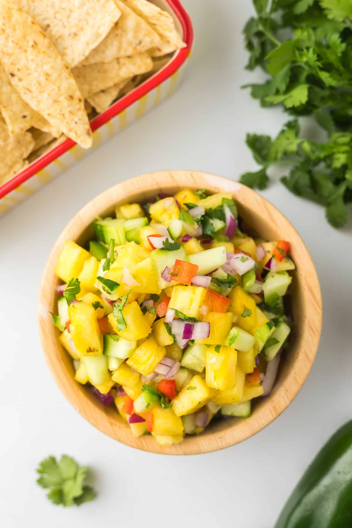 Jalapeno Pineapple Salsa in a wooden bowl with chips and cilantro.