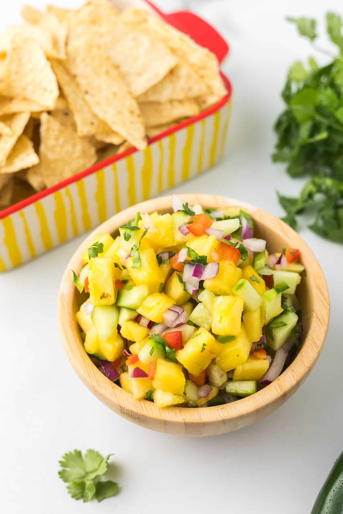 Jalapeno Pineapple Salsa in a wooden bowl with cilantro and chips.