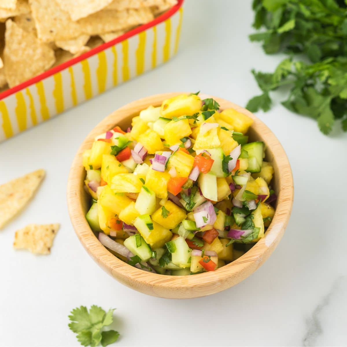 Pineapple salsa in a wooden bowl with cilantro and chips.
