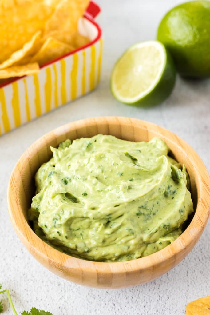 Avocado Cream Sauce in a dish with limes and chips.