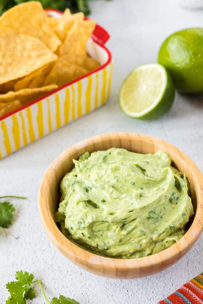 Creamy avocado sauce in a wooden bowl with chips and limes.