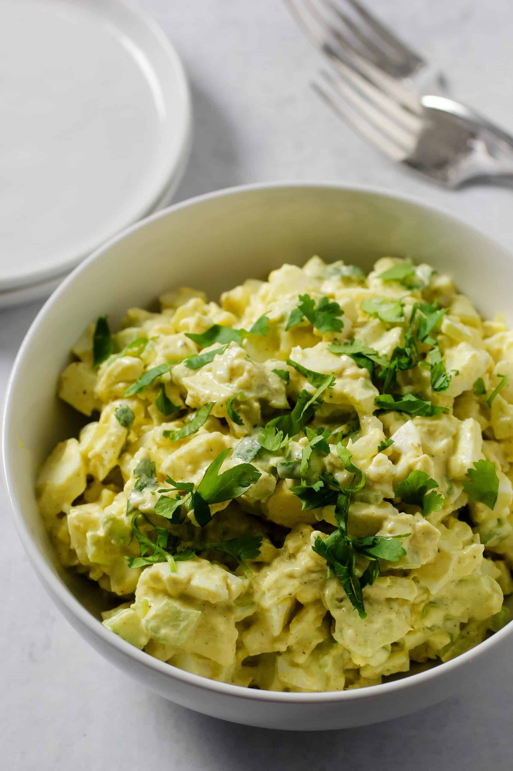 Egg salad in bowl with cilantro on top and plates and silverware.