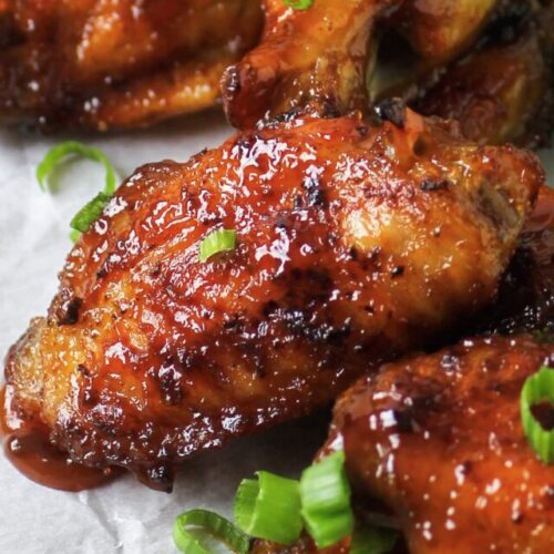 Honey bourbon chicken wings on plate with celery and green onions.