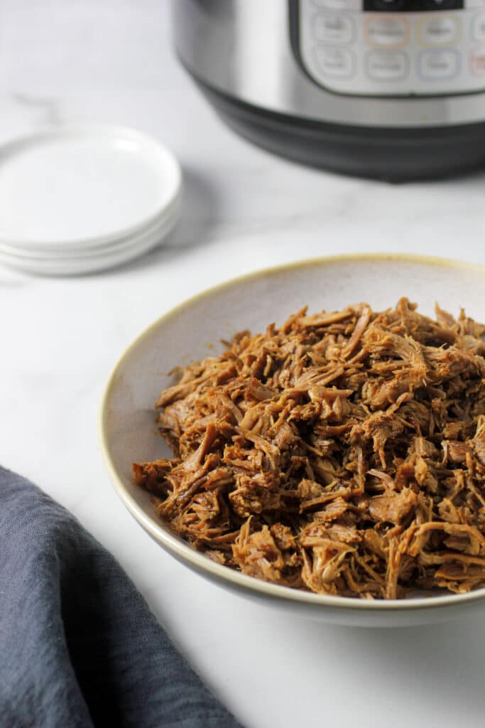 pulled pork in bowl with instant pot behind and two plates
