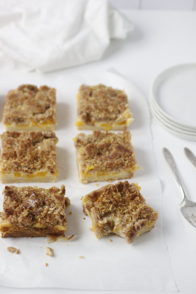 peaches and cream bars cut and placed on parchment paper with two forks and plates to serve