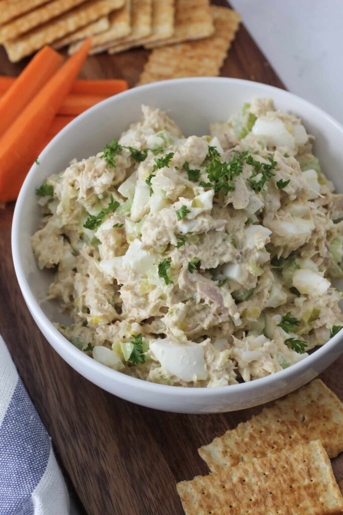 tuna salad with eggs, celery, onion, sweet relish and mayo in bowl with parsley on top.