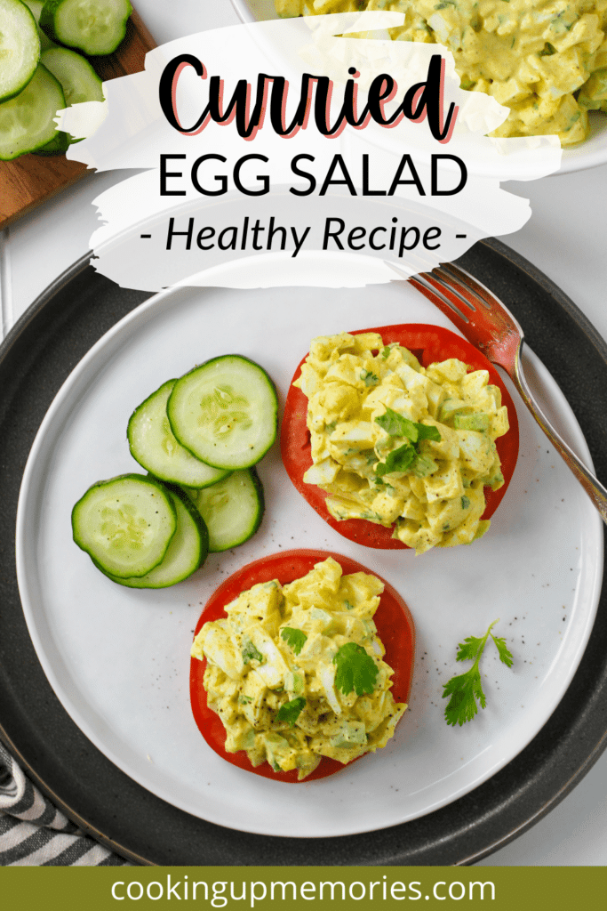 Egg salad on sliced tomatoes with cucumber and a fork on white plate.