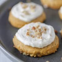 two pumpkin pecan cookies iced with butter cream and sprinkled with pecans on a gray plate