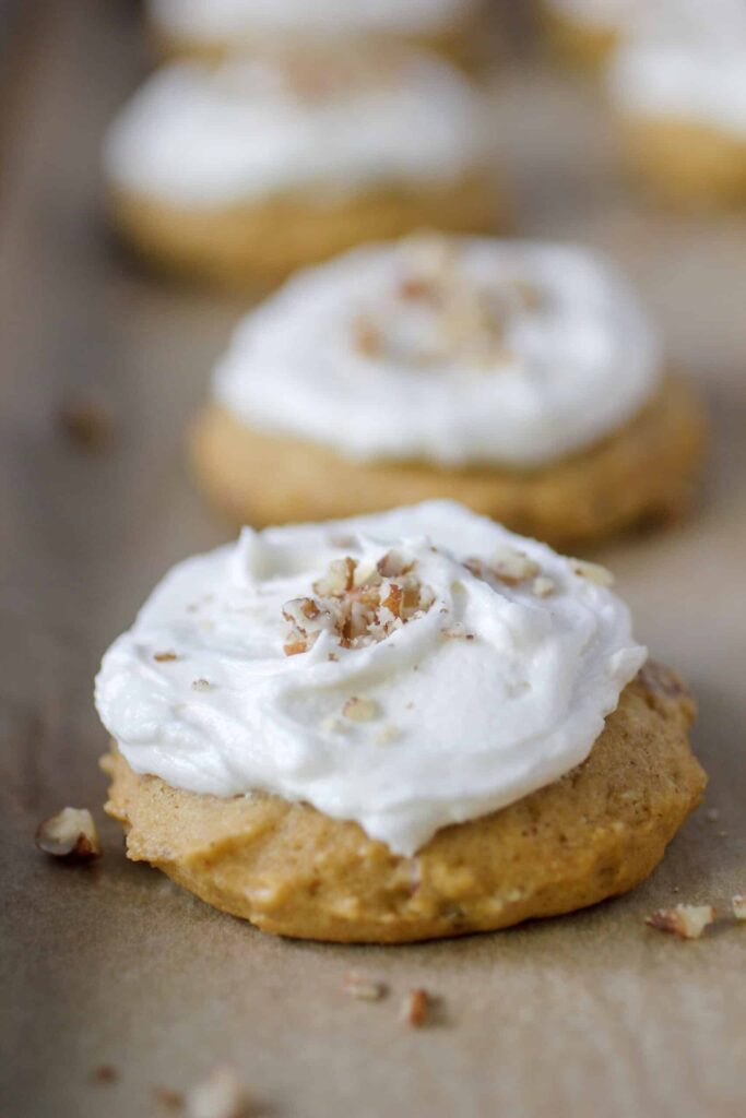pumpkin cookies with icing and nuts on cookie sheet with parchment paper