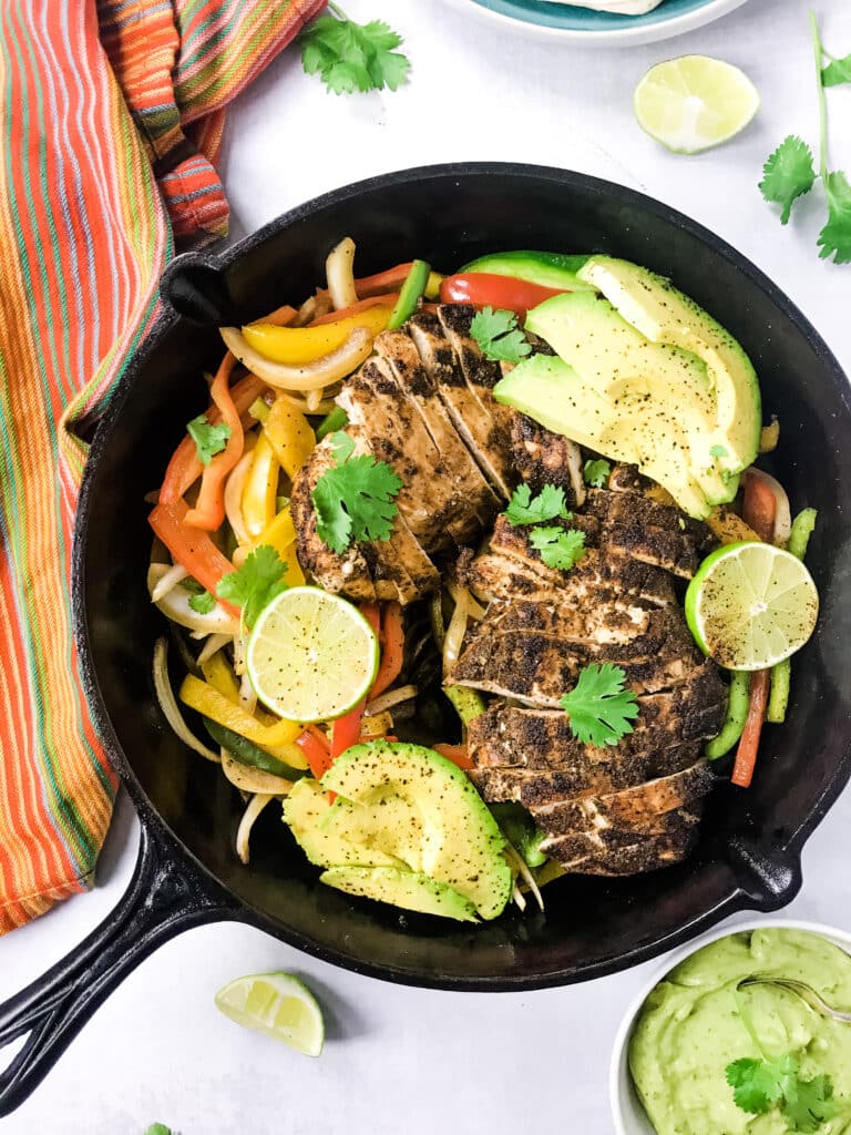 bell peppers, fajitas chicken, lime, avocado and cilantro in black skillet with dish towel