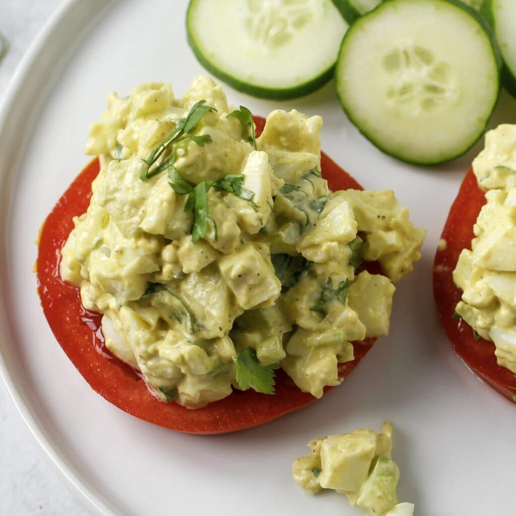 curried egg salad on sliced tomato with cucumbers on a white plate