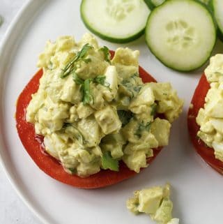 curried egg salad on sliced tomato with cucumbers on a white plate