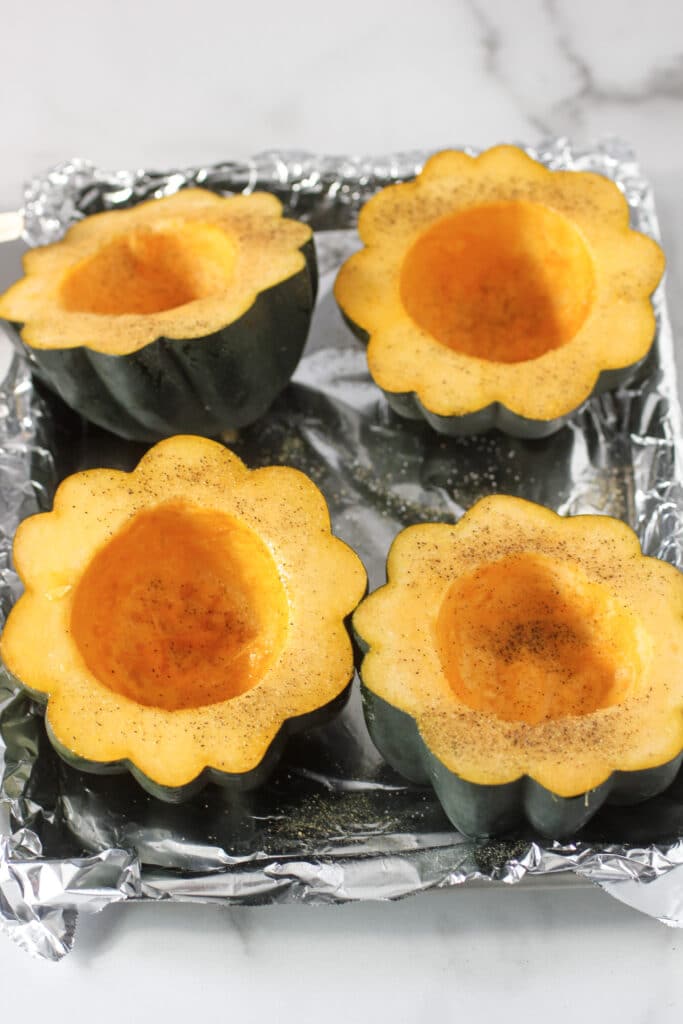 acorn squash on aluminum foil with salt and pepper and ready to be baked.