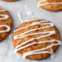 cinnamon sugar coated cookie with icing drizzled over the top on parchment paper with other cookies