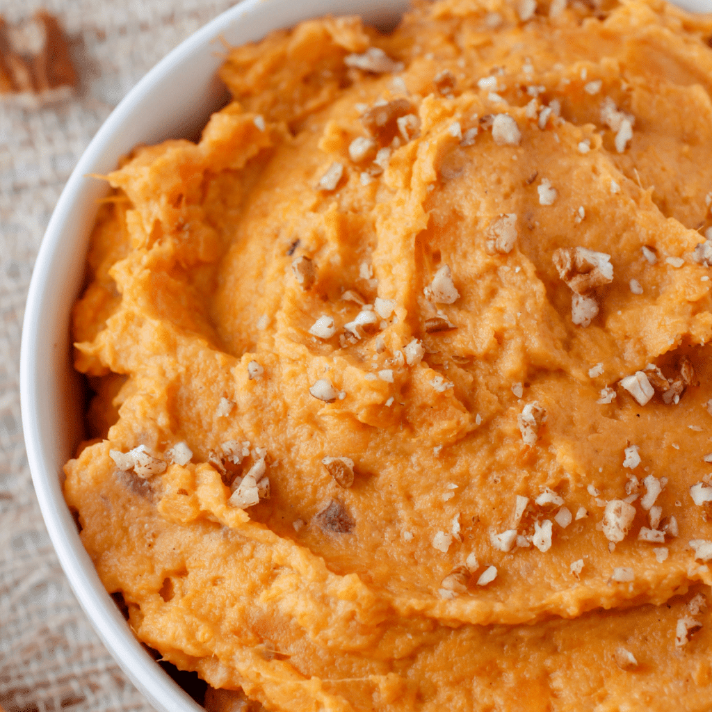 the best mashed sweet potatoes in a bowl topped with chopped pecans