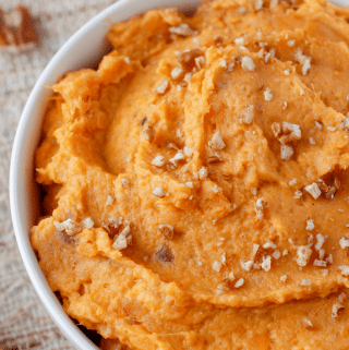 the best mashed sweet potatoes in a bowl topped with chopped pecans