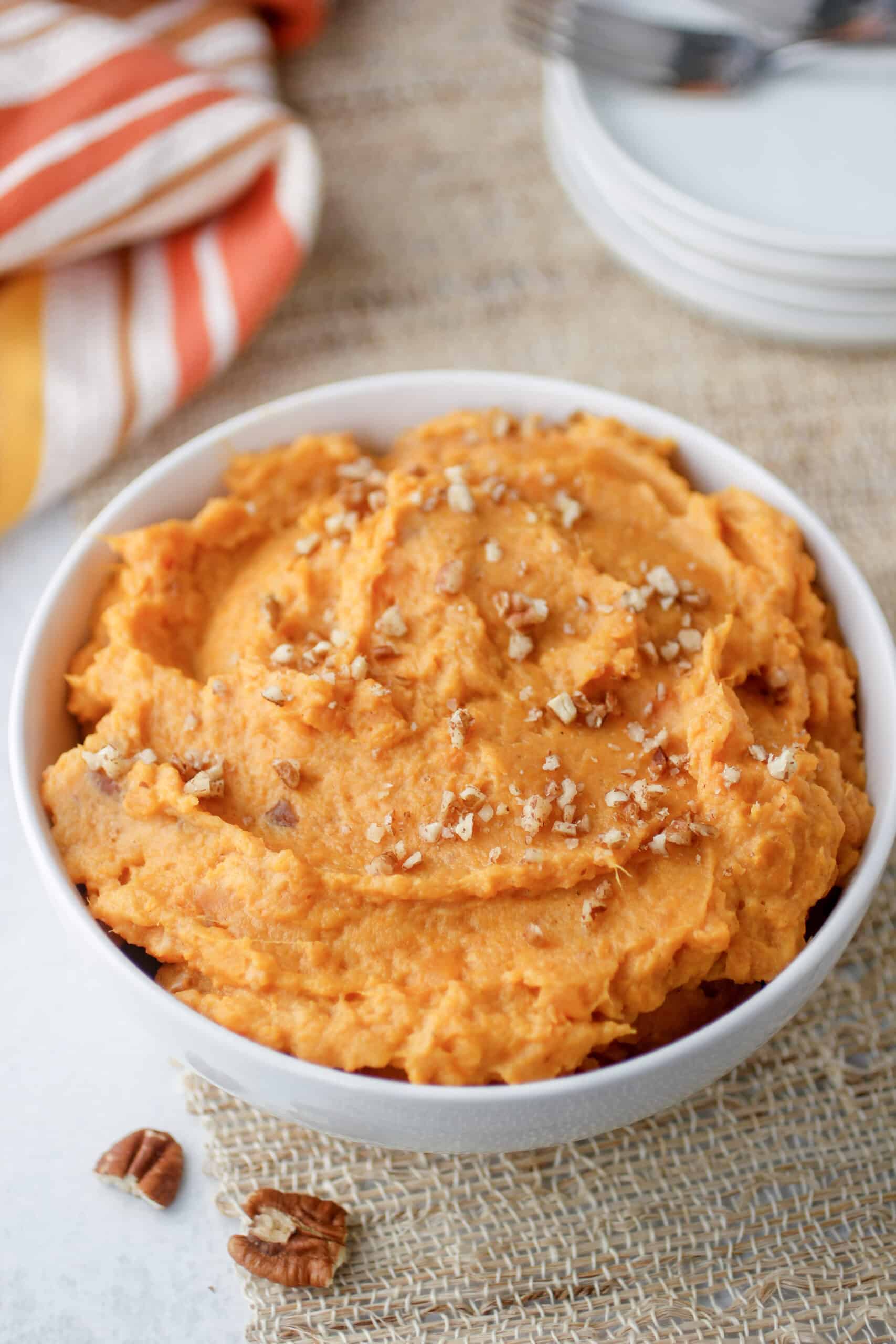 Mashed sweet potatoes with pecans in a serving dish with napkin and plates.