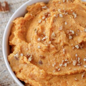 mashed sweet potatoes in serving bowl with pecans sprinkled on top