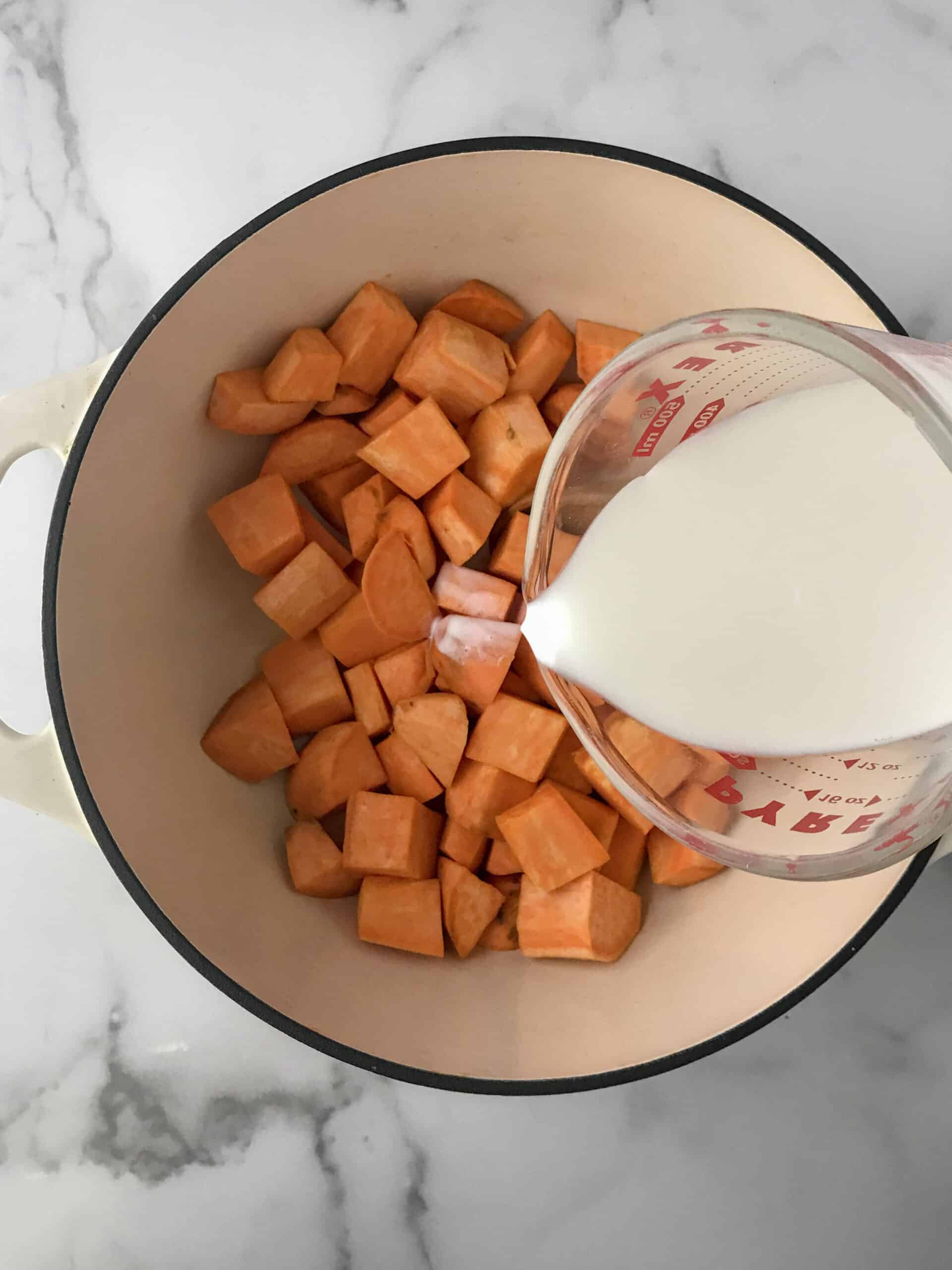 Cut sweet potatoes in Dutch oven with milk being poured into the pot.