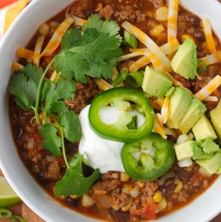 taco soup in bowl with avocado, cilantro, sour cream, cheese and jalapenos as garnish