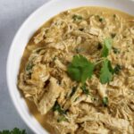instant pot salsa verde chicken in a white bowl with cilantro on top and avocados on the side
