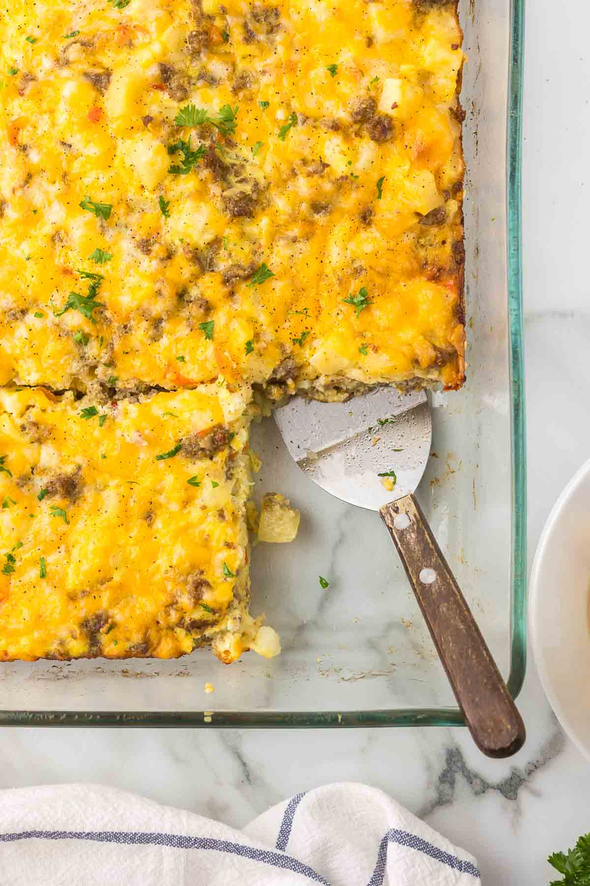 Breakfast casserole in a clear baking dish with a serving spatula.