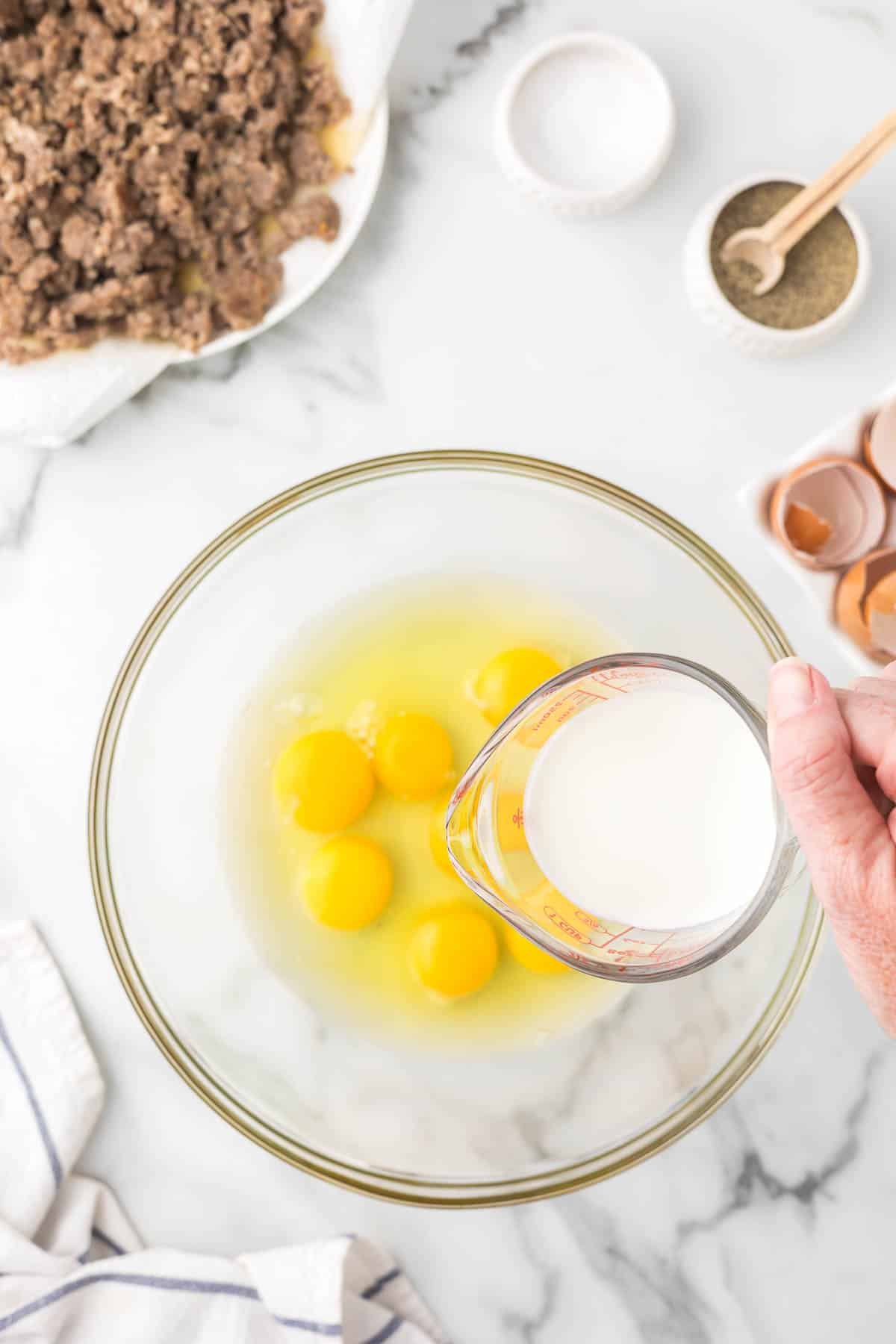 Eggs and milk being added to a clear bowl.