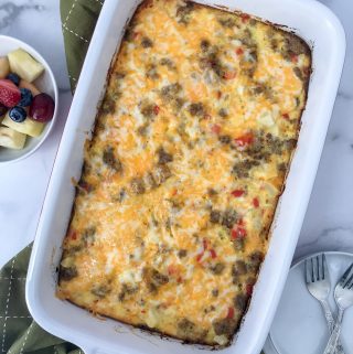 cheesy breakfast casserole in casserole dish right out of the oven with fruilt and plates