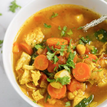 Tuscan Soup with carrots, chicken, celery, chickpeas in a flavorful sauce in a white bowl garnished with fresh parsley