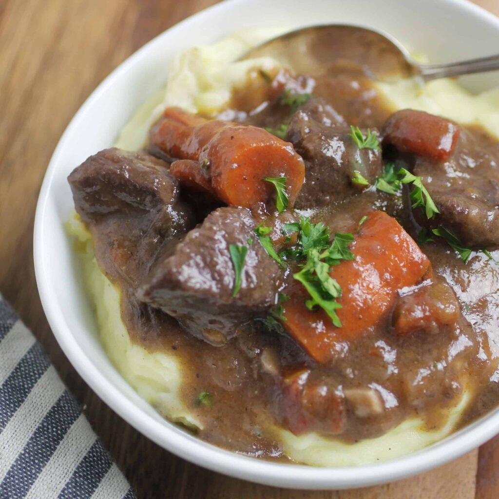 red wine beef stew in a bowl served over mashed potatoes