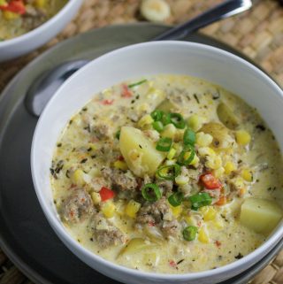 Corn Chowder with sausage, potatoes and bell peppers with green onions on top with spoon and chowder crackers