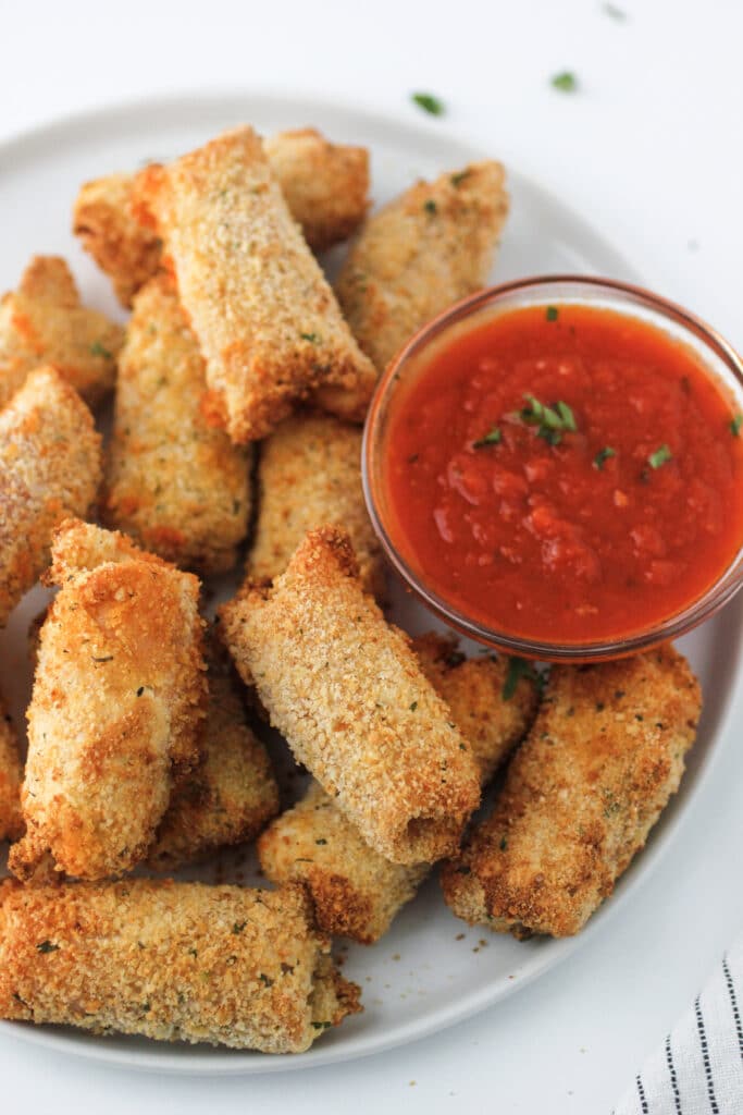 Airy Fryer Cheese Sticks on a plate with a small bowl of marinara for dipping.