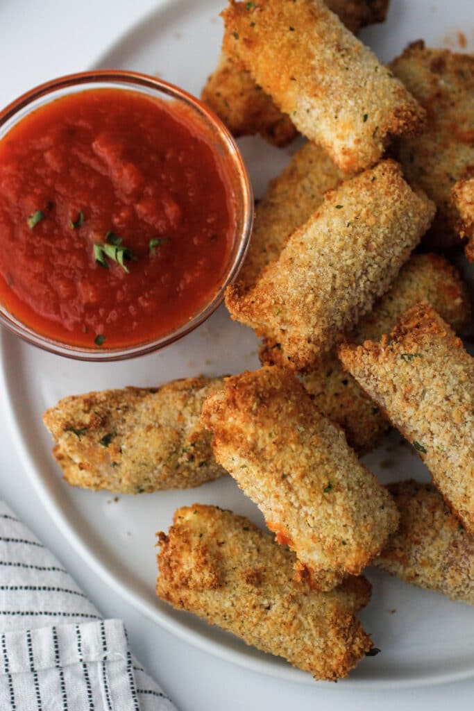 air fryer cheese sticks with marinara in a small bowl on a white plate with a striped napkin