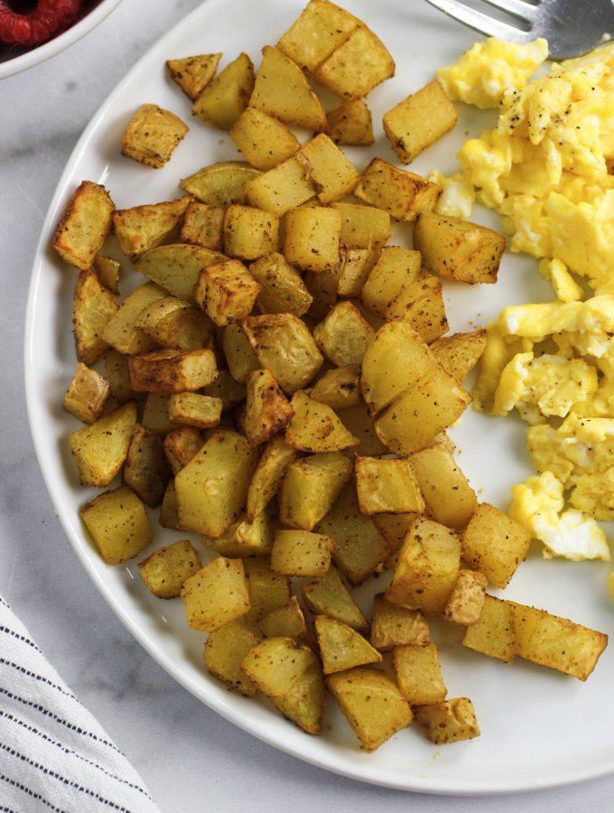 airy fryer potatoes on a white plate with scrambled eggs