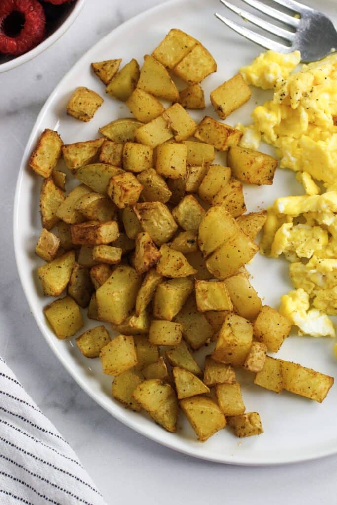 Airy fryer potatoes on a white plate with scrambled eggs.