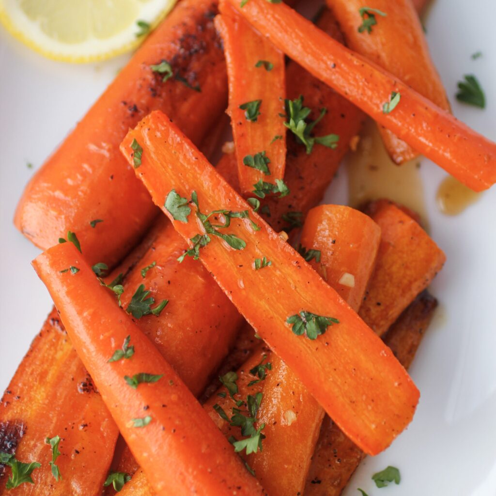 Maple Glazed Carrots on a white serving tray with a fork and garnished with sliced lemons and fresh parsley
