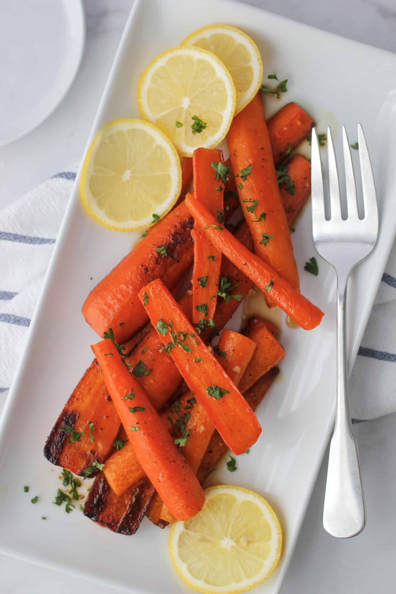 Maple roasted carrots on a plate with lemon slices.