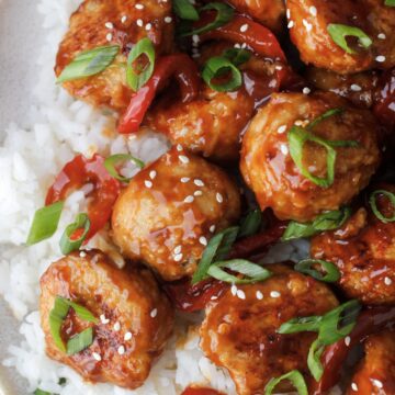 Meatballs with orange chicken sauce and sesame seeds and green onion over white rice with red bell peppers