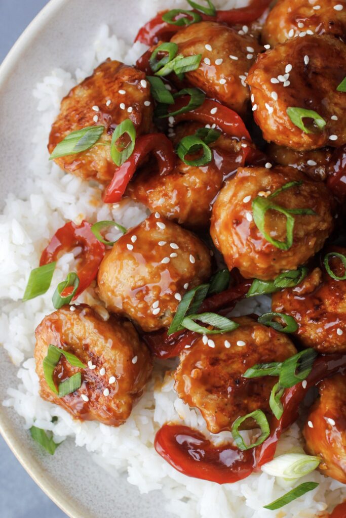 orange chicken meatballs served over rice with green onions and toasted sesame seeds as garnish