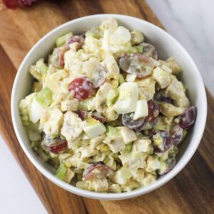 chicken salad with grapes, hard boiled eggs and vegetables in a white bowl on a cutting board