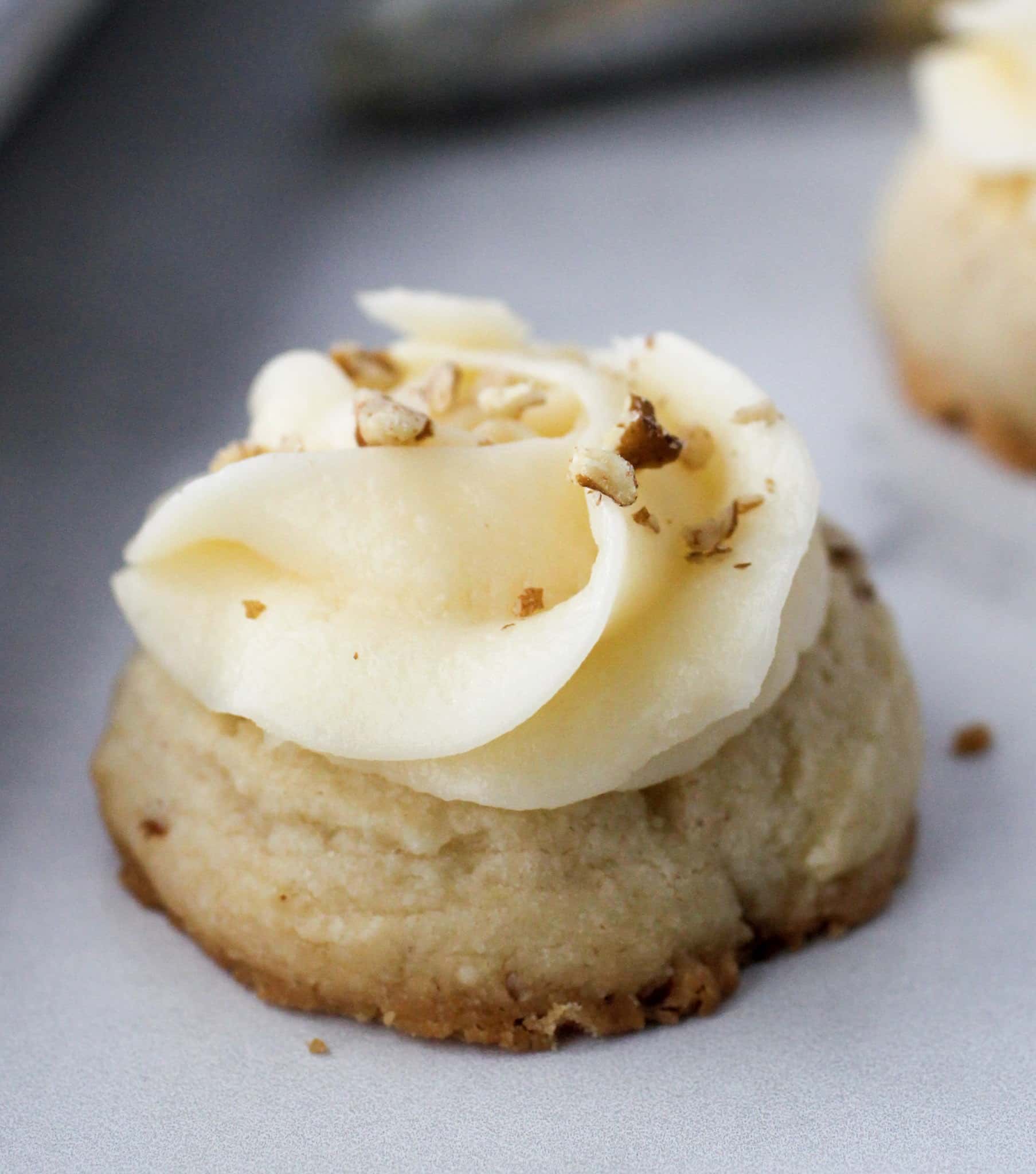 Close-up of a frosted butter pecan thumbprint cookie showing the tender shortbread texture and pecan pieces.