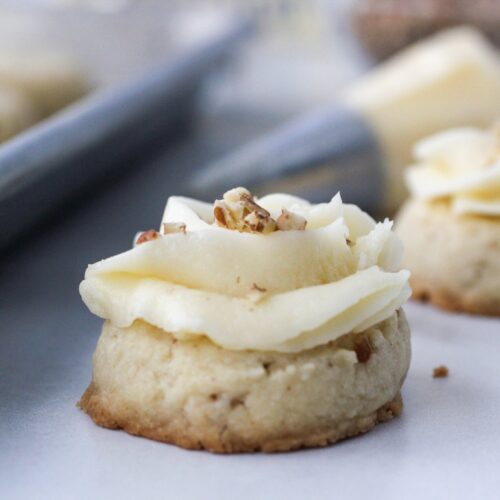 Pecan Thumbprint Cookies with butter cream icing and a sprinkle of pecans on top with a icing bag behind the cookie.