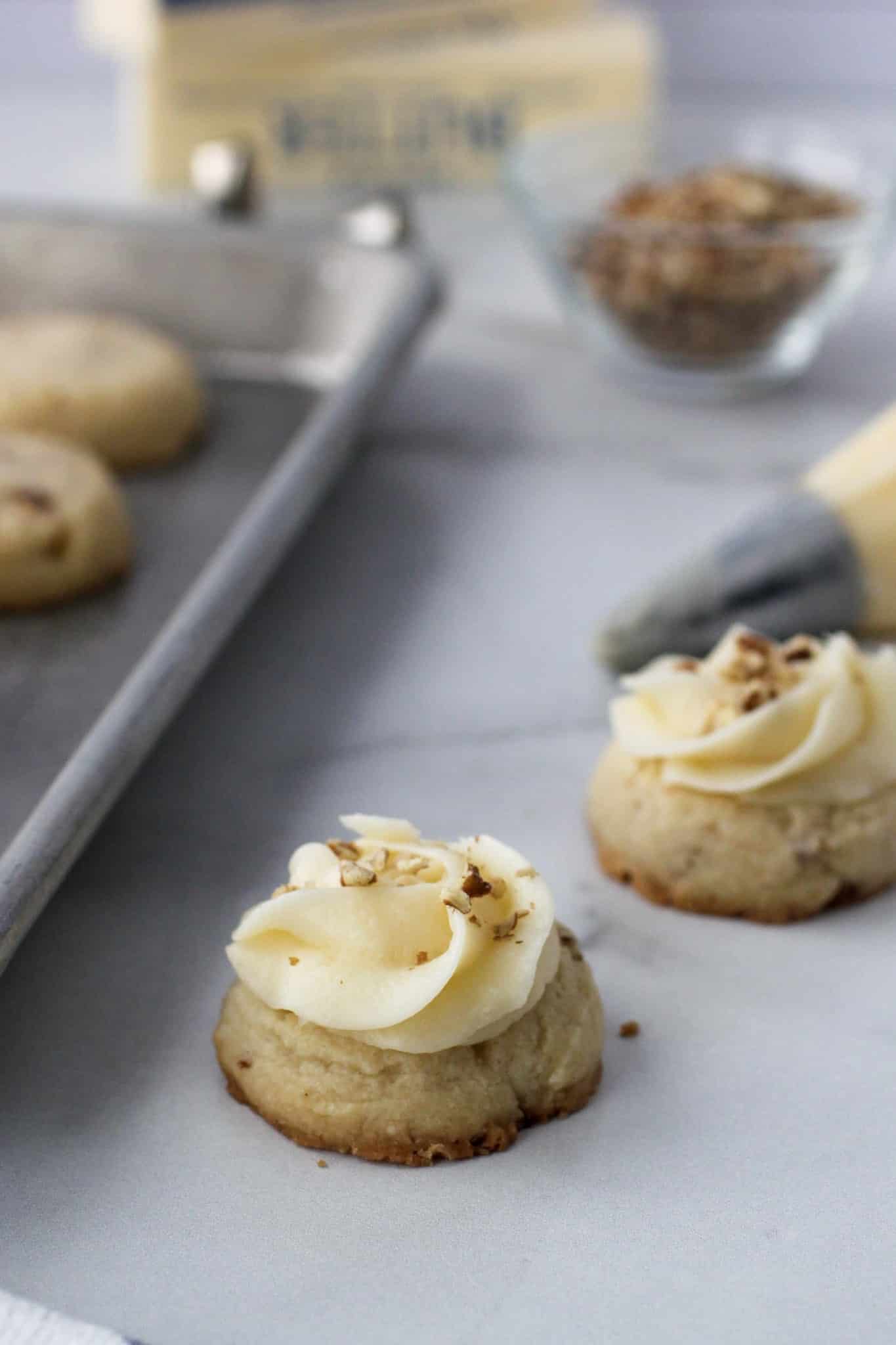 Butter pecan thumbprint cookie with a swirl of buttercream frosting and chopped pecans sprinkled on top.