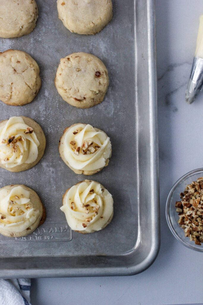 Pecan Thumbprint Cookies on a baking sheet that have buttercream icing and are sprinkled with chopped nuts.
