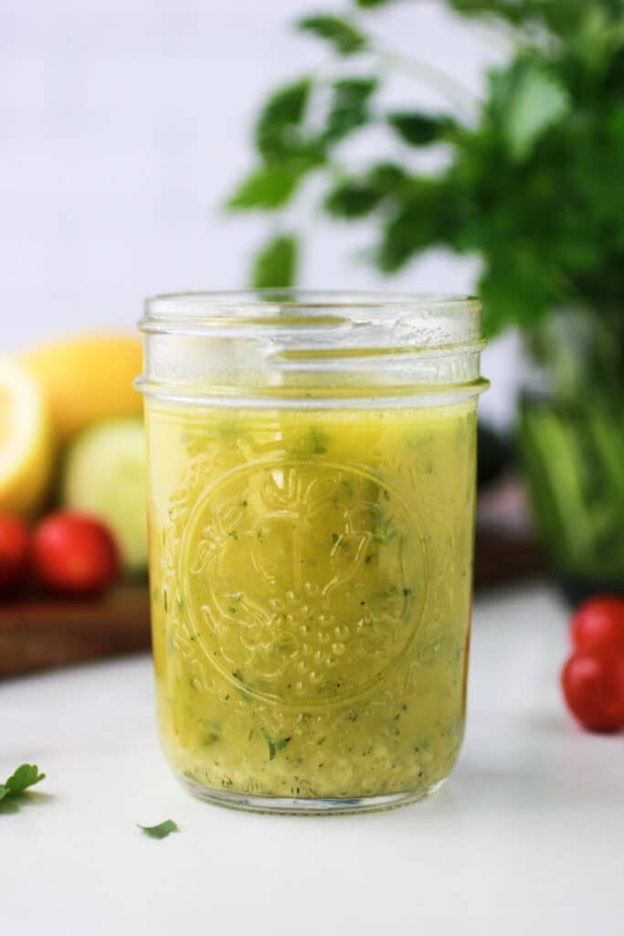 Simple Lemon Vinaigrette dressing in a mason jar with fresh vegetables on a cutting board.
