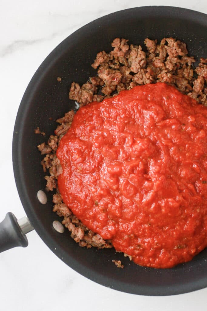 Cooked sausage in skillet with marinara sauce.
